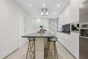 Une cuisine moderne dotée d’un îlot central, de tabourets de bar, d’appareils électroménagers en acier inoxydable et d’un revêtement mural décoratif.