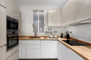 A modern kitchen with white cabinetry, a double sink, stainless steel appliances, and a wooden countertop. - Stylish Stay in Salamanca (Madrid)