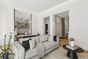Ein modernes Wohnzimmer mit einer Couch, einem Esstisch und einem durch einen offenen Durchgang einsehbarer Küchenbereich.