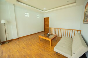 Un salón amplio con piso de madera, una mesa de centro de vidrio, un sofá color beige y barandilla de madera.