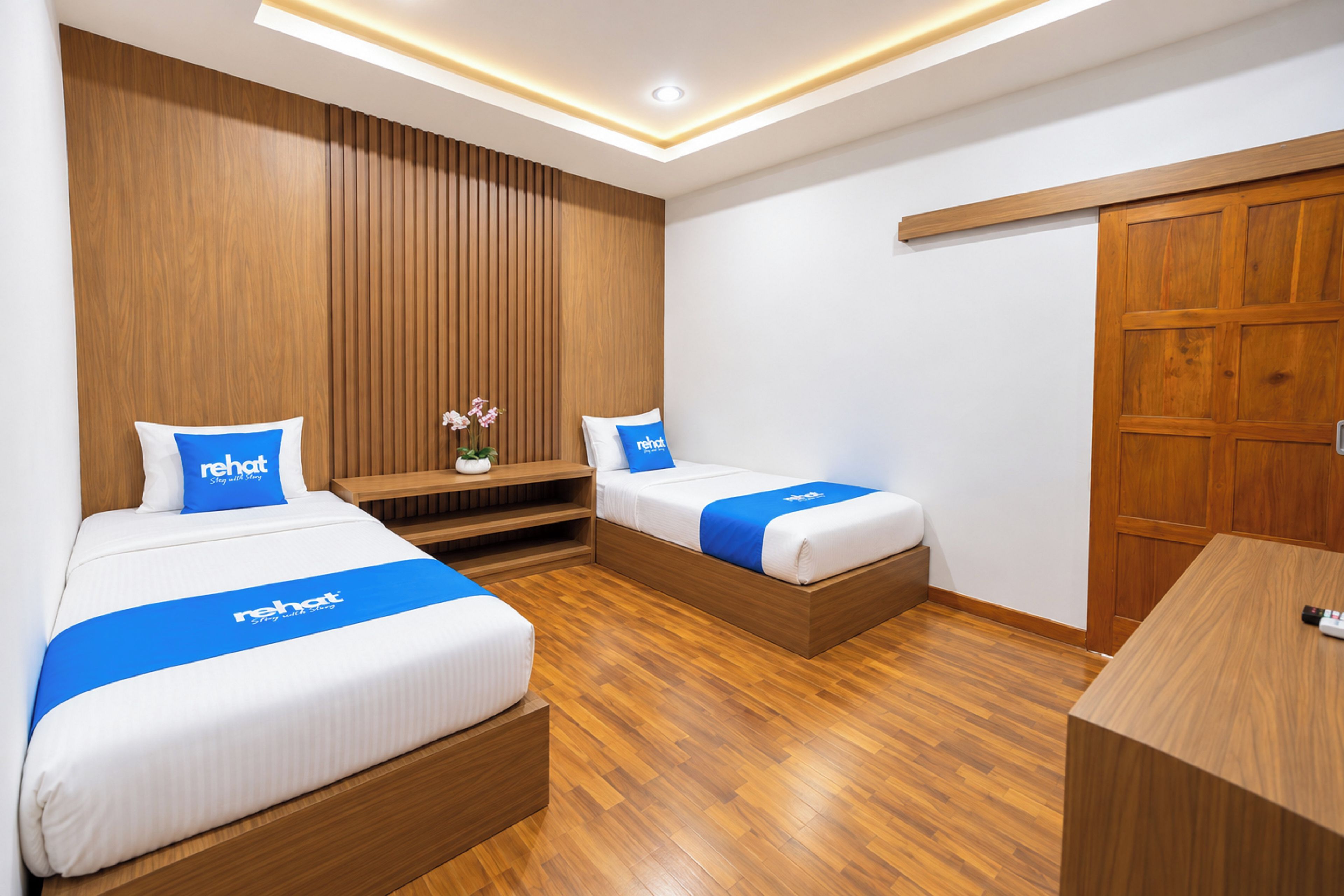 A hotel room with two beds, wooden flooring, a wooden wardrobe, and a small table.