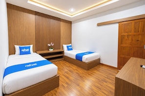 Habitación de hotel con dos camas, suelo de madera, un armario de madera y una pequeña mesa.