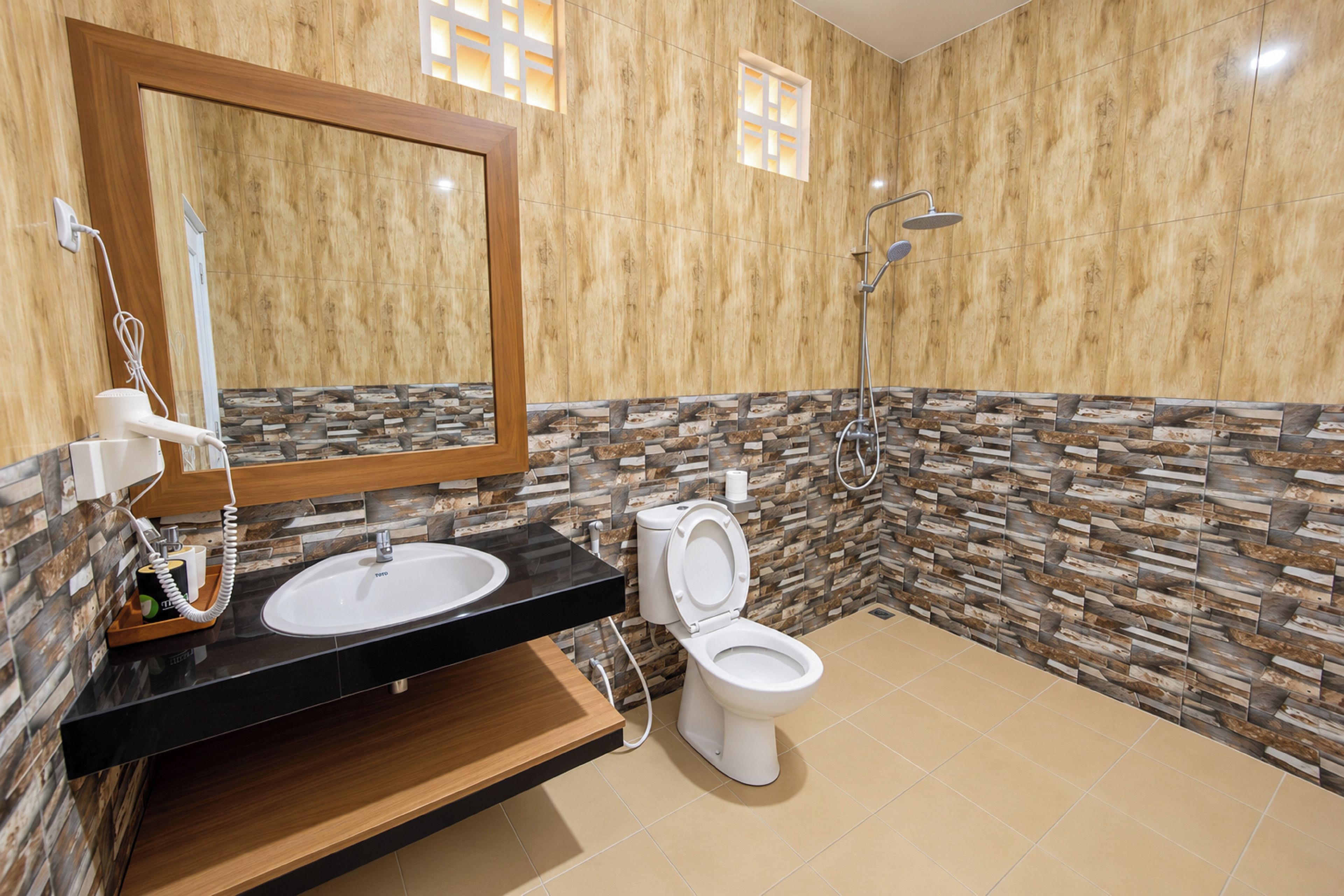 A modern bathroom with a wooden vanity, a white toilet, a shower with a handheld showerhead, and a mirror with a wooden frame.