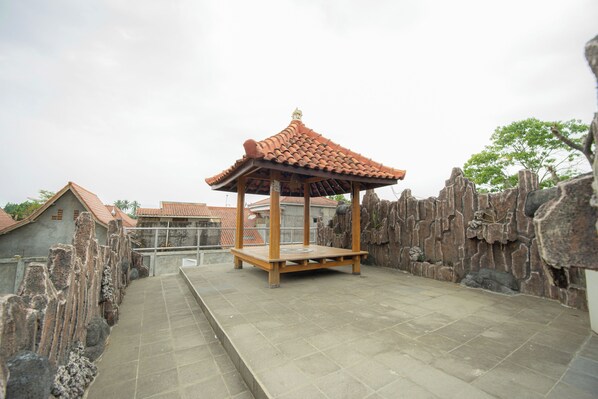 A traditional pavilion with a tiled roof, surrounded by stone walls and a paved walkway.