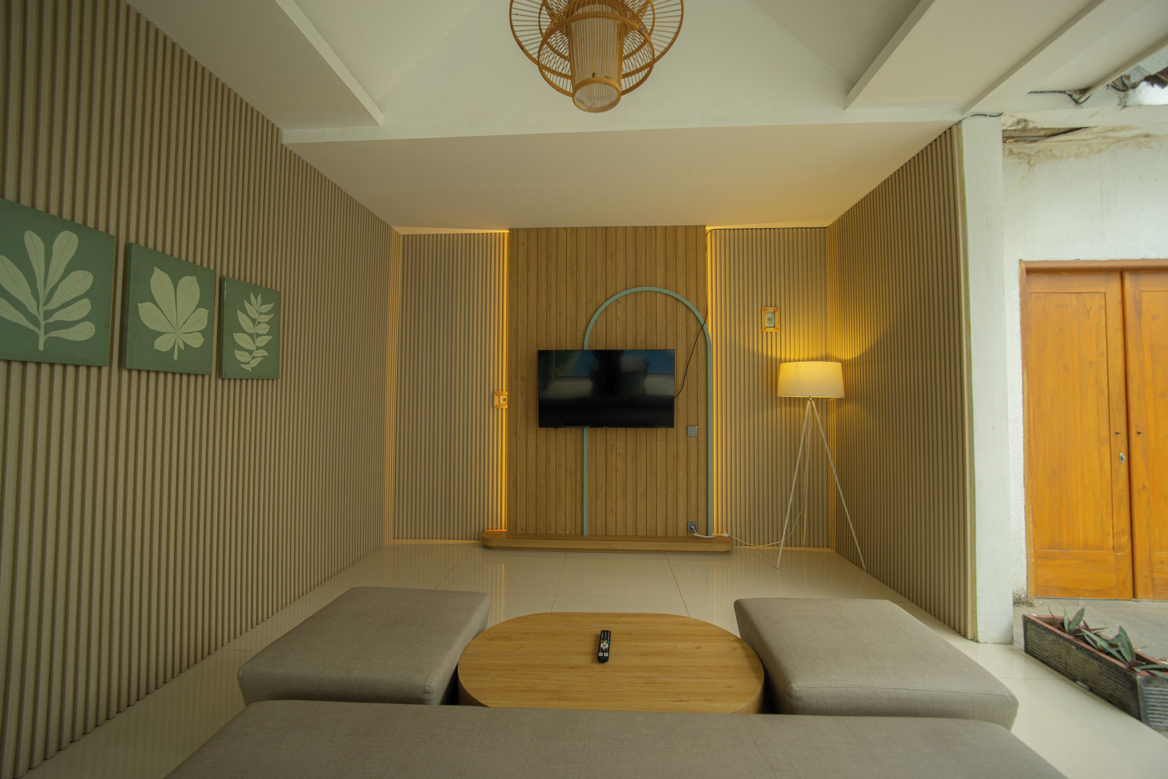 A modern living room with a flat-screen TV mounted on a wooden panel wall, a round coffee table, and two cushioned seating areas.