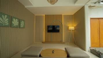 A modern living room with a flat-screen TV mounted on a wooden panel wall, a round coffee table, and two cushioned seating areas.