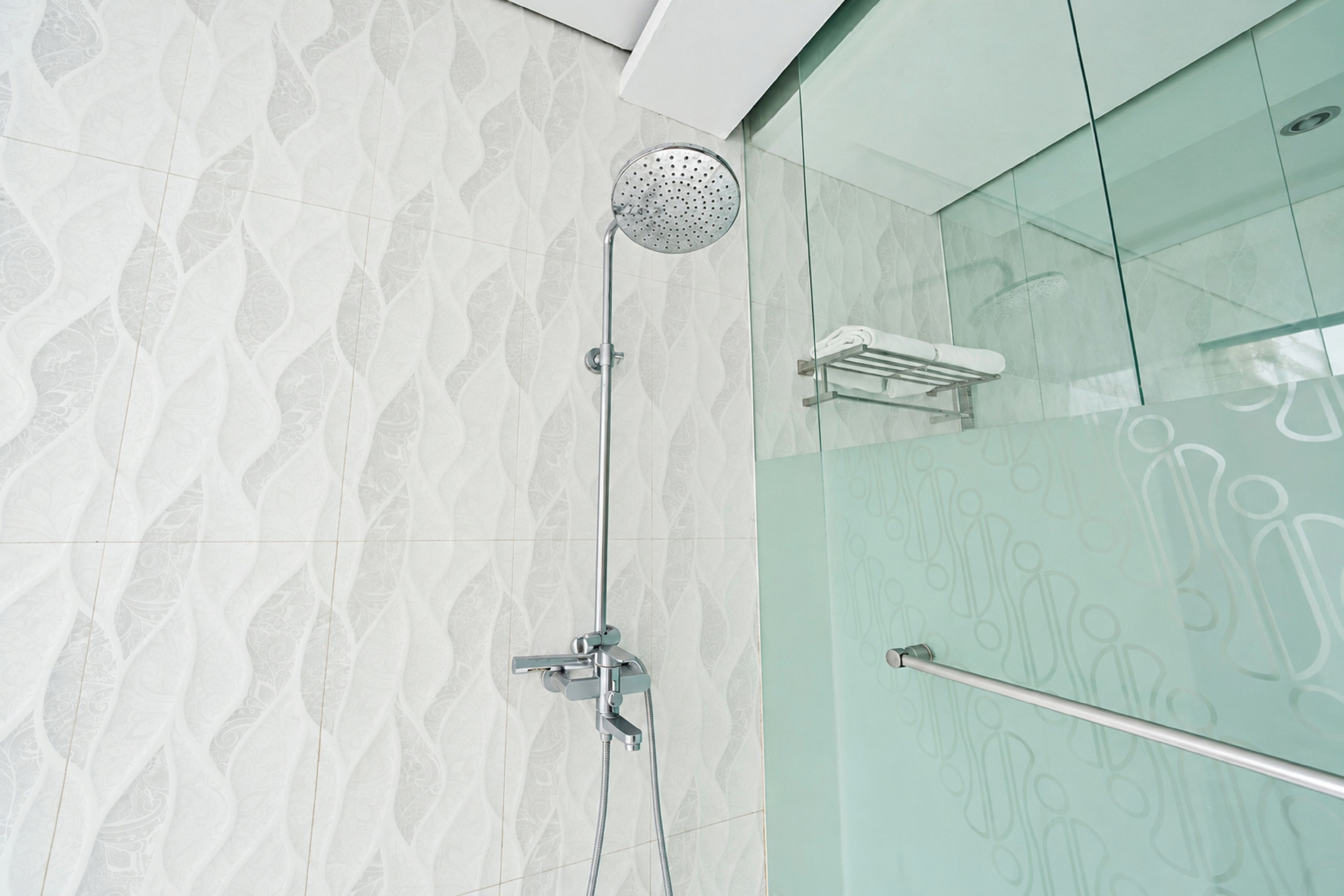 Une douche moderne dotée d’un pommeau de douche à pluie, d’un pommeau de douche à main et d’une cabine de douche en verre.
