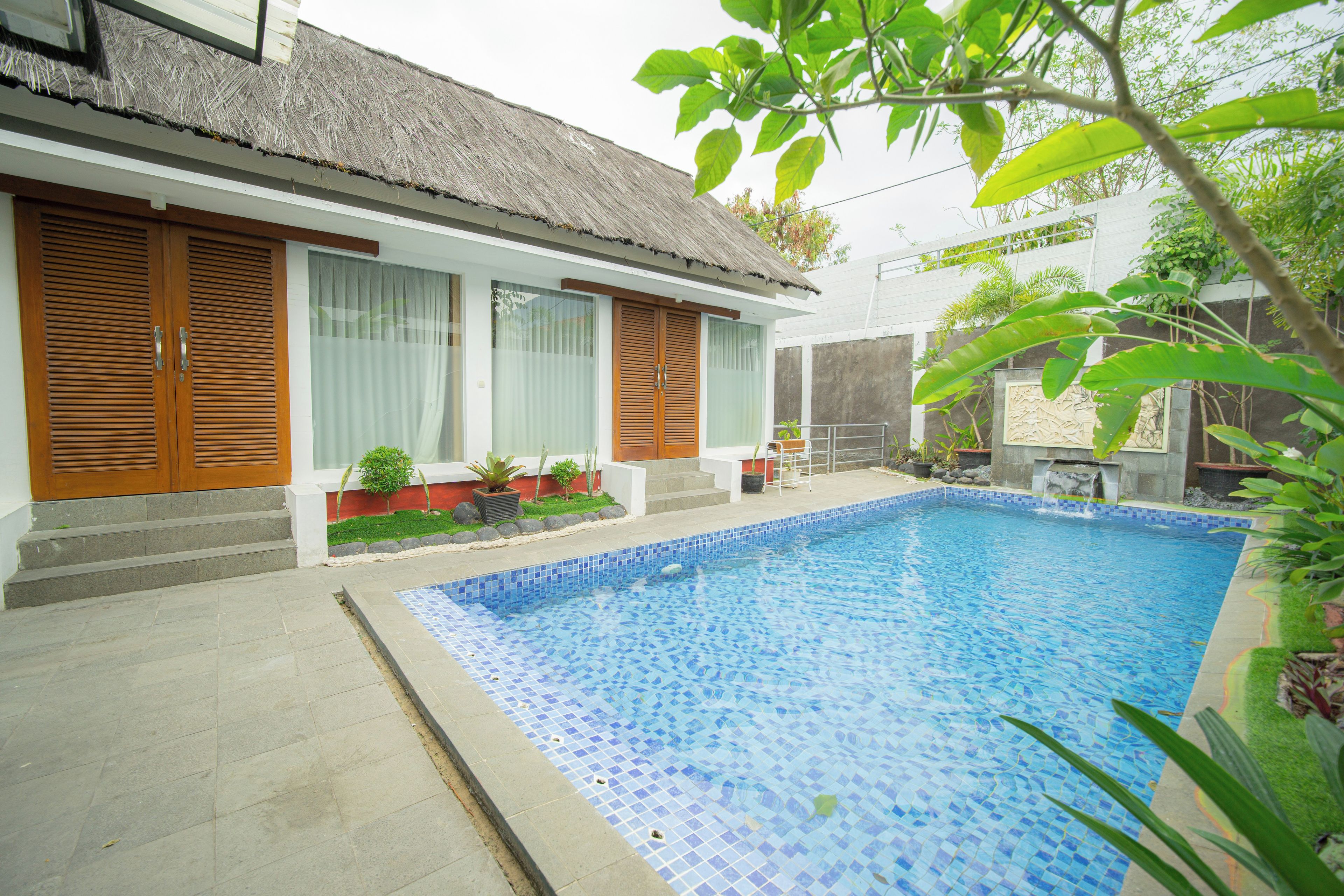 A residential property with a swimming pool, a thatched roof, and a garden with potted plants.