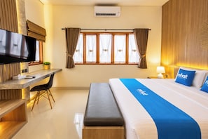 Habitación de hotel con cama, escritorio, silla, televisor y ventana con cortinas.