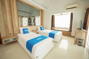 A hotel room with two beds, a large window with curtains, an air conditioning unit, and a trash bin.