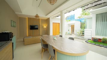 Une cuisine moderne dotée d’un îlot central, d’un coin repas avec une table et des chaises, et offrant une vue sur le jardin extérieur.
