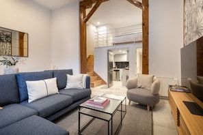 A modern living room with a sofa, armchair, coffee table, and a TV on a wooden stand. - Madrid Duplex | Barrio de las Letras (Madrid)
