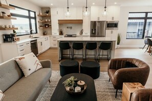 Eine moderne Küche mit weißen Schränken, einer zentralen Kochinsel mit Barhocker und einem Essbereich mit einer Couch und Stühlen.