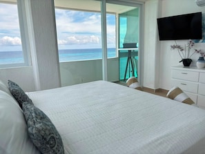 A hotel room with a large bed, a TV mounted on the wall, and a view of the ocean. - Oceanfront Loft, Hotel District - At Oleo Resort (Cancún)