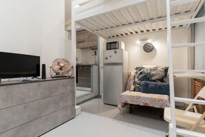 A compact living space with a kitchenette, a bed with a floral bedspread, and a television on a stand. - GuestHost - Cozy Apartment in Downtown Milan (Milan)