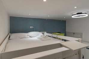 A modern bedroom with a bed, a bedside table, a green trash bin, and a ceiling light fixture. - GuestHost - Cozy Apartment in Downtown Milan (Milan)