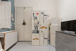 A compact room with a white door, a flat-screen TV on a grey cabinet, and a white desk with a telephone. - GuestHost - Cozy Apartment in Downtown Milan (Milan)