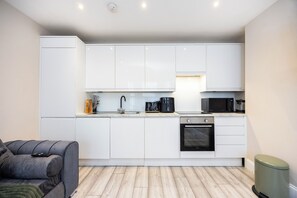 Una cocina compacta con gabinetes blancos, horno integrado y microondas.