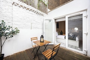 A small, private outdoor space with a wooden table and chairs, a potted plant, and a sliding glass door leading to a bedroom with a bed and a nightstand. - Comfy & Spacious|2 Bedroom Apartment|Seconds from Hammersmith Central Station (London)