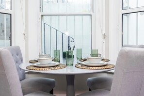 Una mesa de comedor con platos, tazones y vasos, rodeada de sillas tapizadas.