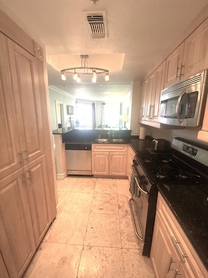 A kitchen with wooden cabinets, a stainless steel microwave, a stove, and a dishwasher. - Luxury Las Vegas Strip!  2BR Condo ~ Sphere view ~ 24/7 Pool 3-24 (Las Vegas)