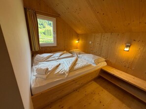 A wooden room with a bed, a window, and a wall-mounted light fixture. - 012 Mw21b in Murau (Murau)
