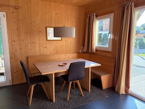 A wooden interior with a table and chairs, a bench, a hanging light fixture, and a window with curtains. - 012 Mw21b in Murau (Murau)