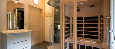 Un baño moderno con tocador blanco, cabina de ducha de vidrio y estantería de madera.