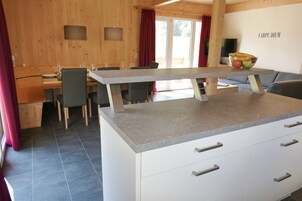 Cocina moderna con isla central, comedor con sillas y vistas al exterior.