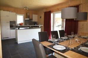A modern kitchen with a central island, dining table set for six with chairs, and a view of the outside through a window. - 002 MW5 in Murau (Murau)