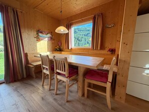A wooden interior with a dining table, chairs, a window with curtains, a hanging light fixture, and a refrigerator. - 011 Mw21a in Murau (Murau)