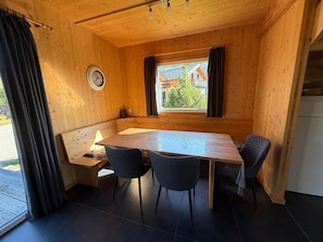 A wooden cabin interior with a dining table, two chairs, a clock, and a window with curtains. - 014 Mw23 in Murau (Murau)