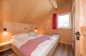 Ein Zimmer mit Holzwänden, einem Bett, einem Fenster mit rotem Vorhang und einer Tür mit Schloss.