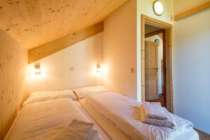 A room with two beds, wooden beams on the ceiling, and a door leading to another room. - 006 Mw13 in Murau (Murau)