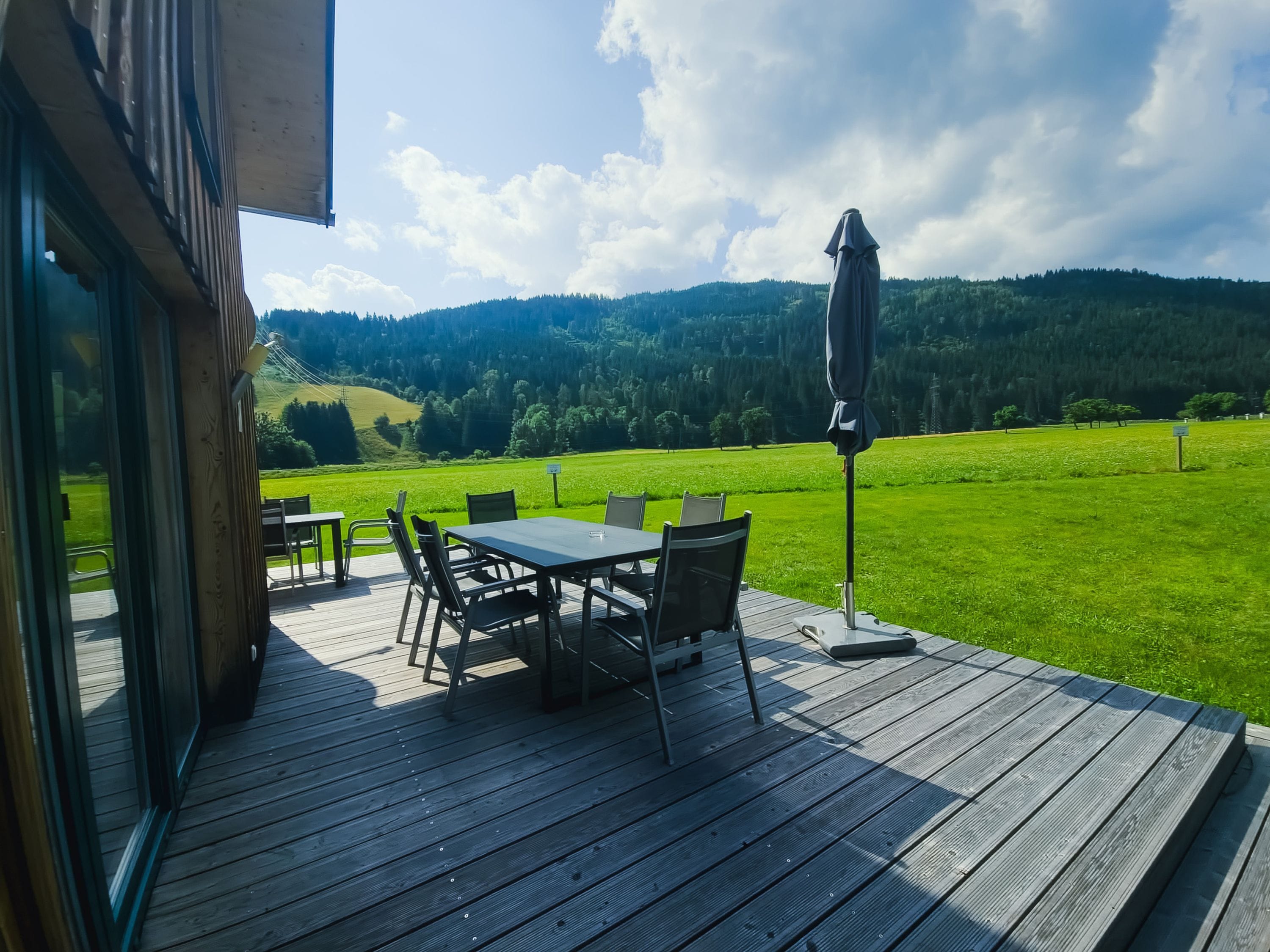 Una terraza exterior con mesa y sillas, con vistas a un campo verde y colinas boscosas.