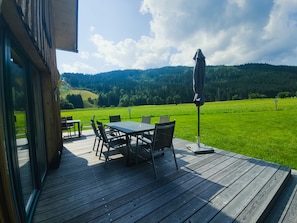 An outdoor deck with a table and chairs, overlooking a green field and forested hills. - 006 Mw13 in Murau (Murau)