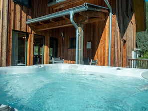 Una cabaña de madera con un jacuzzi, un área de estar techada y una puerta de vidrio que da al interior.