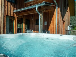 Una cabaña de madera con un jacuzzi, un área de estar techada y una puerta de vidrio que da al interior.