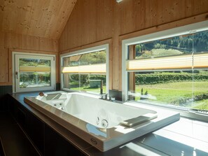 Un baño moderno con una bañera grande, techo de madera y amplios ventanales con vistas a un paisaje verde.