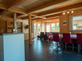 Un interior de madera con comedor con sillas rojas, cocina con campana de acero inoxidable y un ventanal con cortinas.