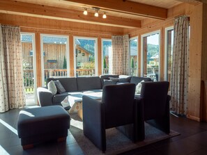 Una sala de estar moderna con sofá, sillas y una mesa de centro. Amplias ventanas ofrecen vistas al exterior.
