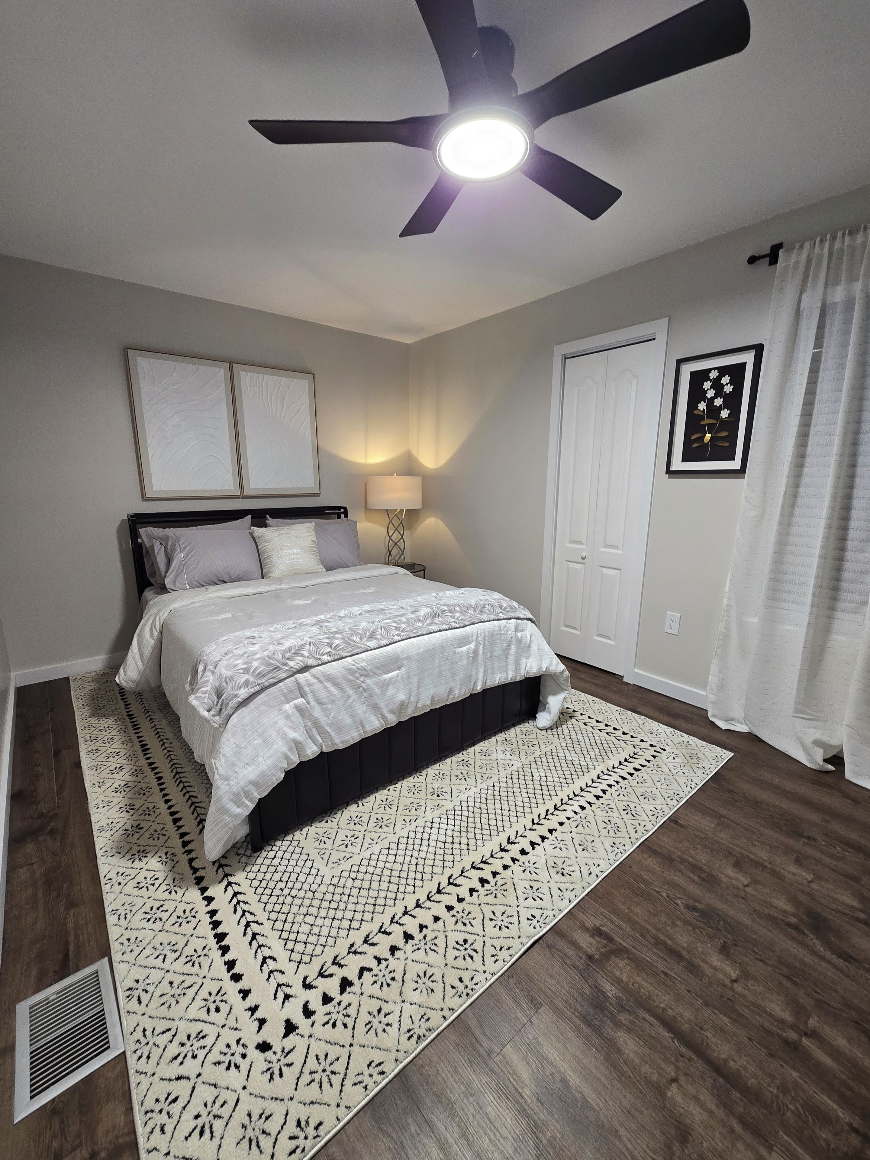 Una camera da letto con un letto, una ventola a soffitto, un comodino, una sveglia a muro e una porta.