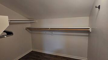Una stanza piccola, scarsamente illuminata, con soffitto spiovente, pavimento in legno e una singola lampada.