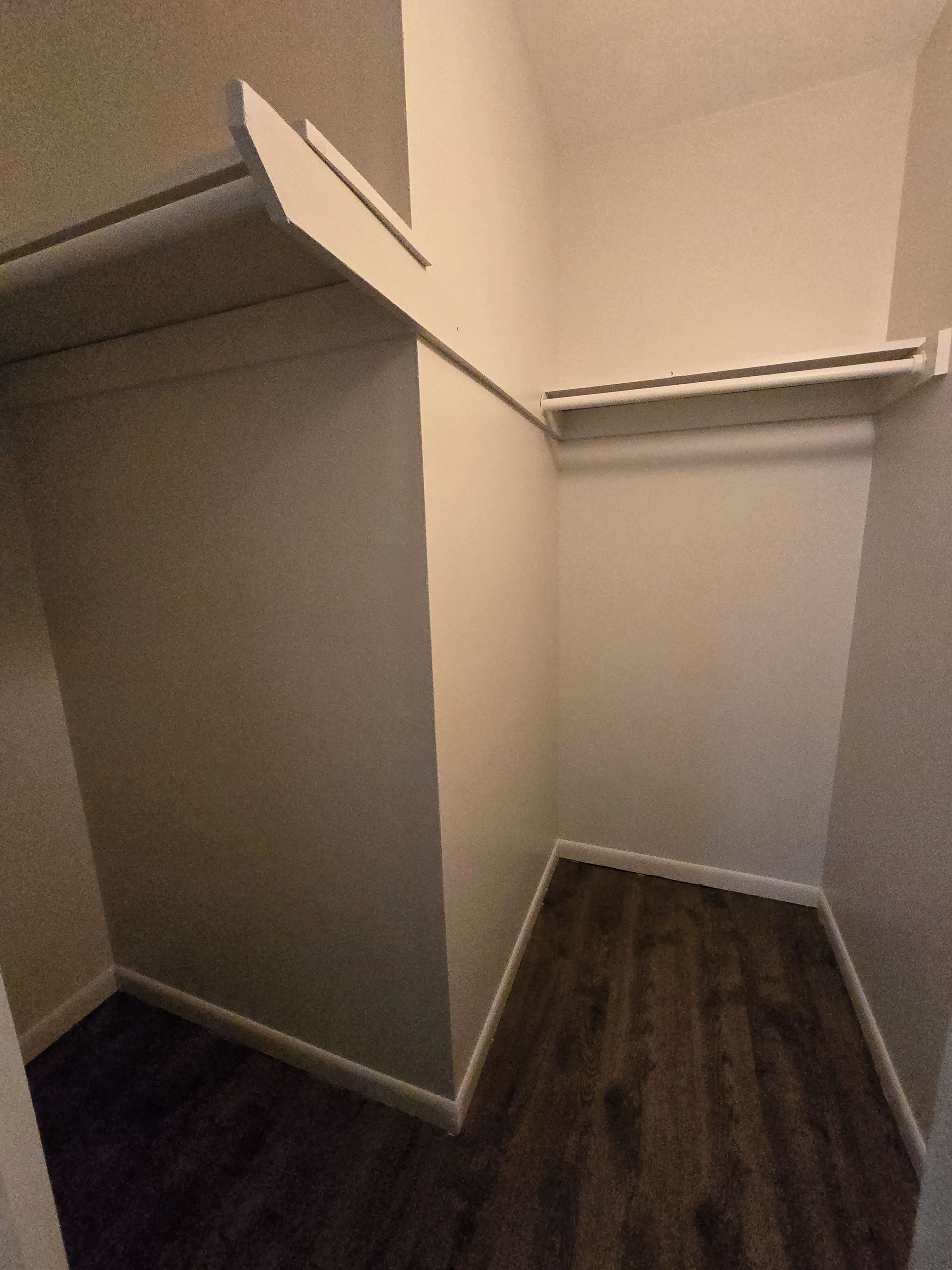 A corner of a room with a dark wooden floor, white walls, and a white closet with a door partially open.