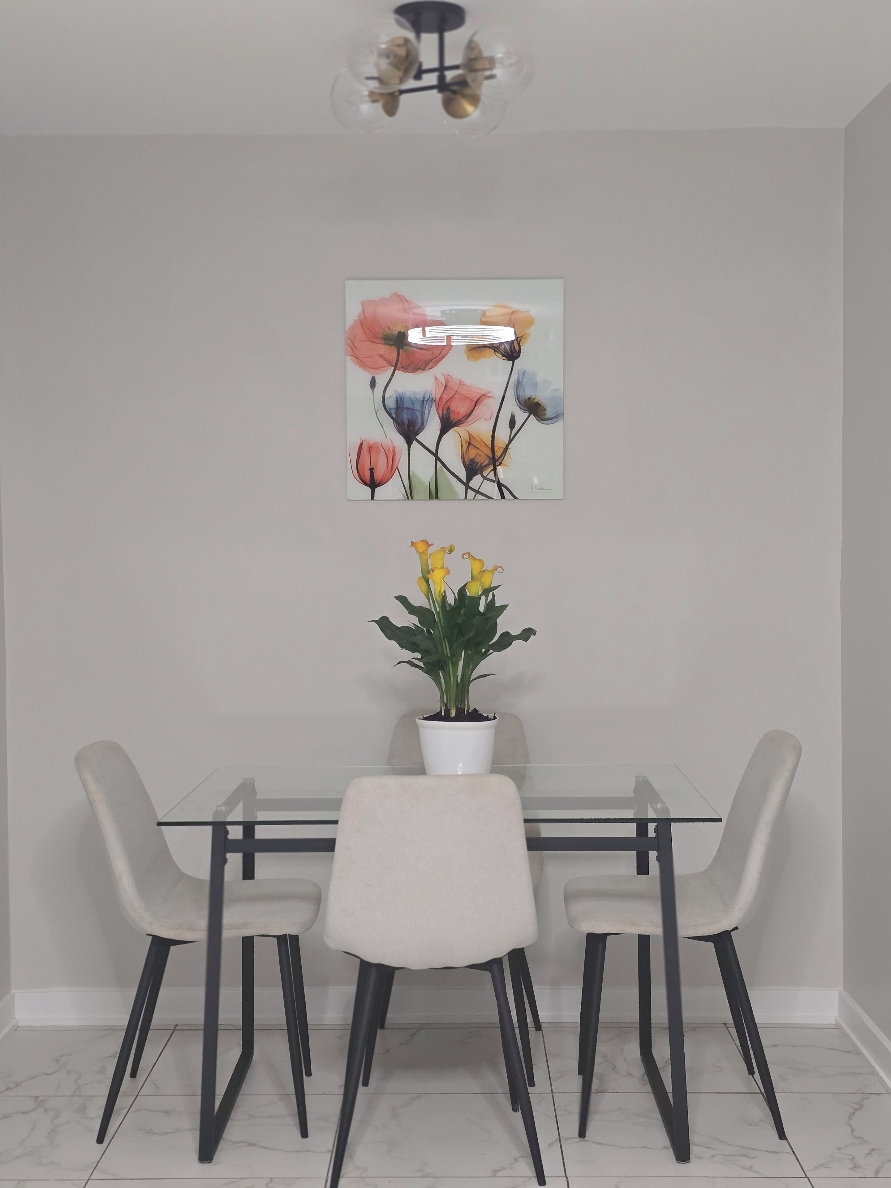 Una zona pranzo con un tavolo in vetro, quattro sedie, una pianta in vaso e un'opera d'arte appesa al muro.