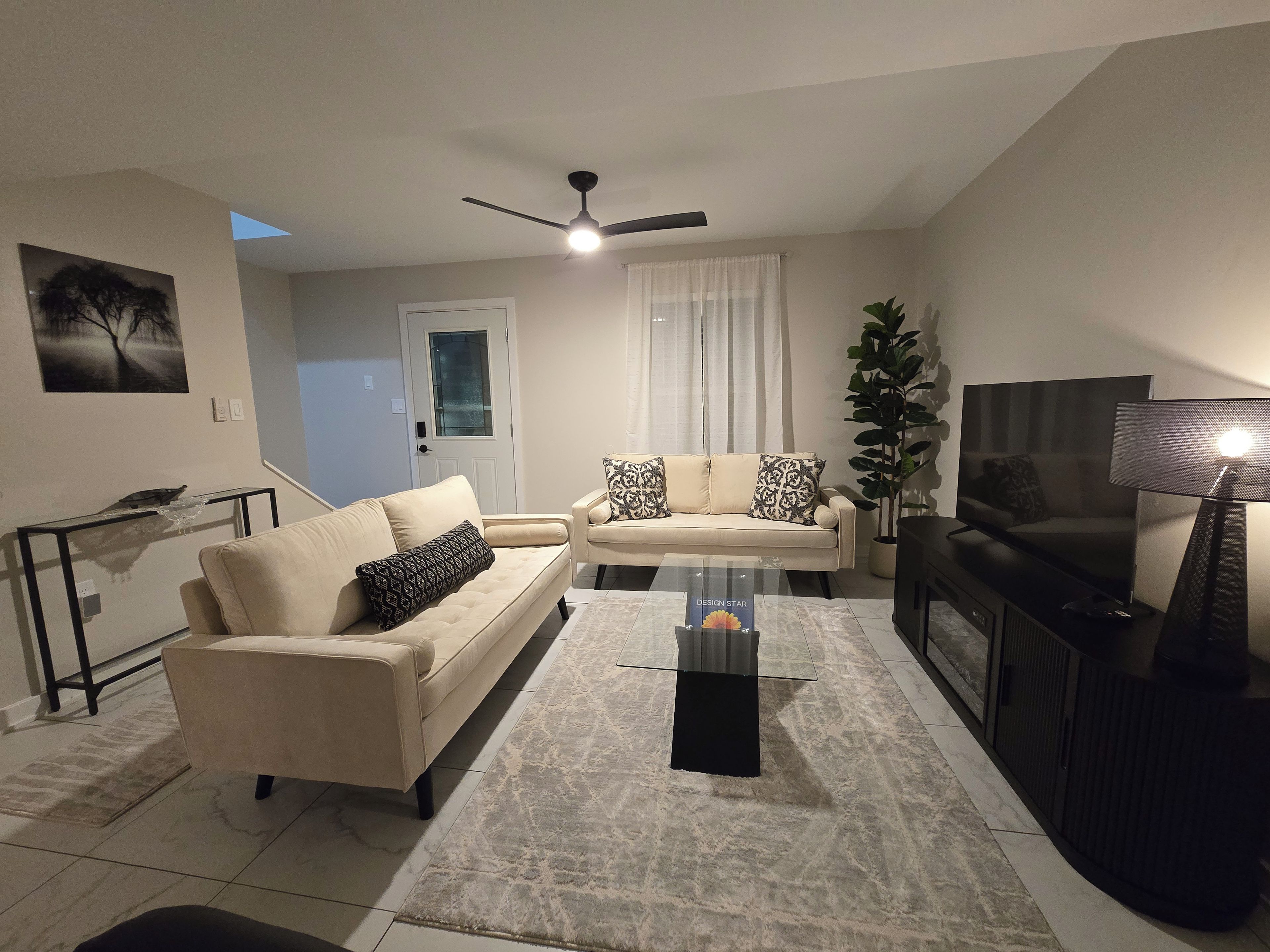 Un soggiorno con divano, tavolino, televisione e ventilatore a soffitto.
