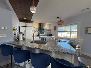 A modern kitchen with granite countertops, a stainless steel sink, and blue bar stools. - Massage Chair! Stay at Love Shack by the Beach -under a block to Park or Beach (Port Clinton)
