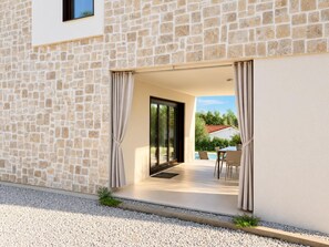 Ein modernes Gebäude mit Stein-Fassade, einem Glastür-Eingang und einer Terrasse mit Gartenmöbeln.