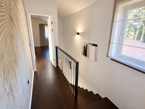 Eine Treppe mit hölzernen Stufen und einem schwarzen Geländer, die zu einem Raum mit Fenster und Wandleuchte führt.