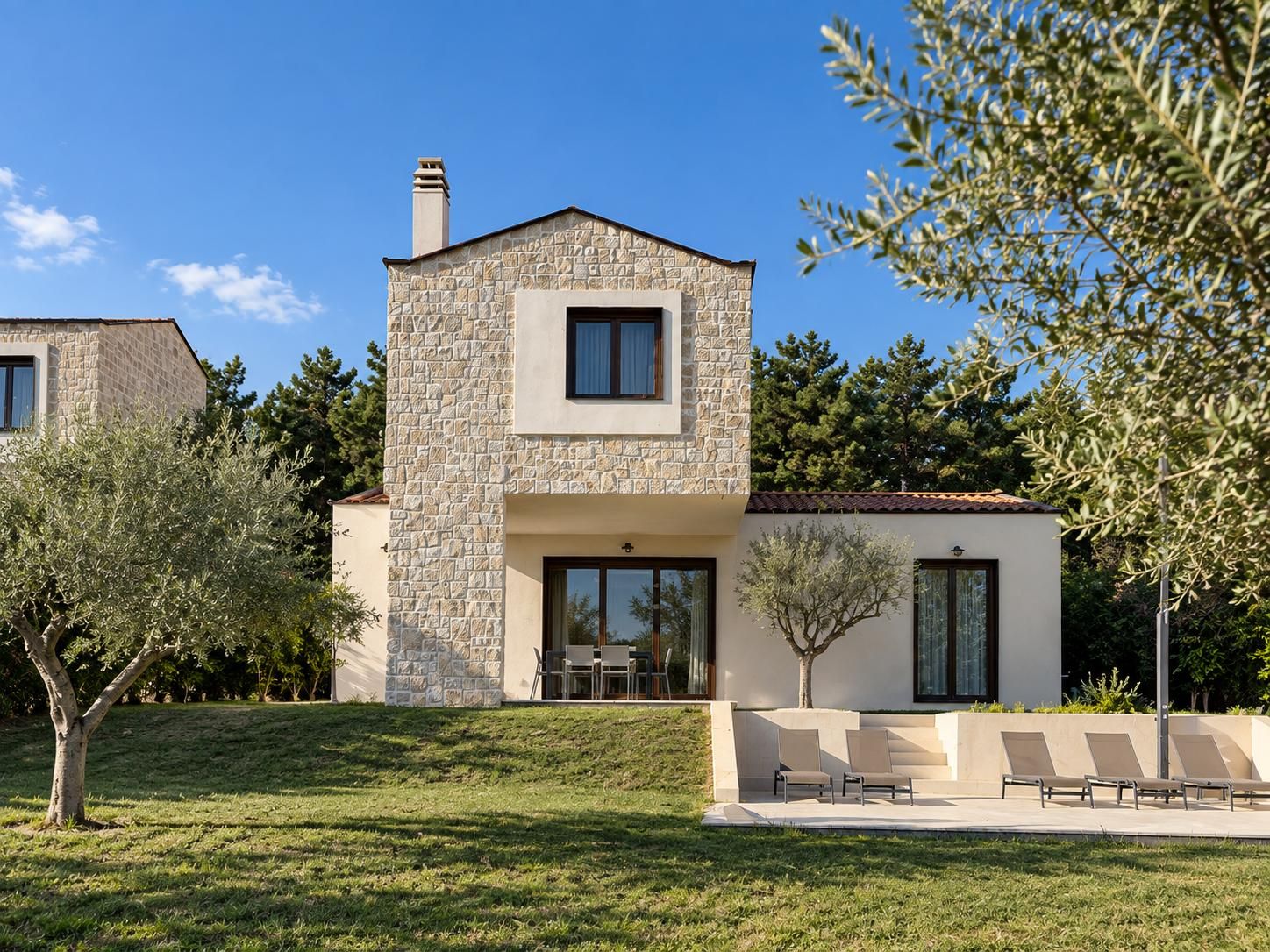 A modern two-story house with a stone facade, a flat roof, and a small balcony with seating.